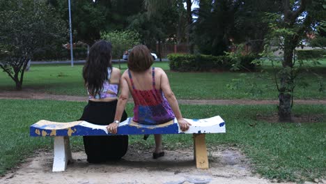 mother and daughter sitting on a bench in the park talking to each other and chilling down