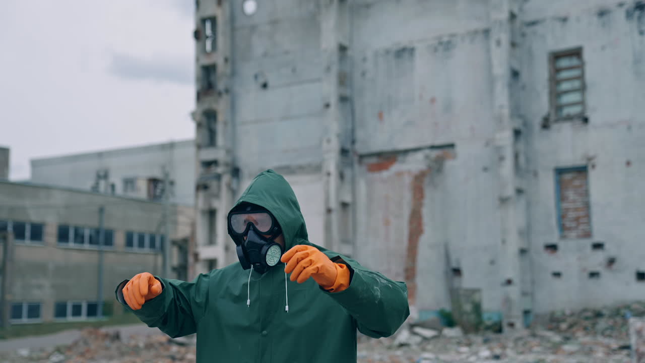 Human survivor standing alone in ruined place. Guy in the gas mask and safety clothes against the background of abandoned building. Apocalypse concept.