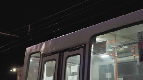 close-up view of an electric tram at night, focusing on the reflective windows and overhead equipment