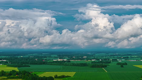 a beautiful aerial timelapse captures shape-changing white cumulus clouds moving across the sky above a vast rural landscape of green agricultural fields in latvia