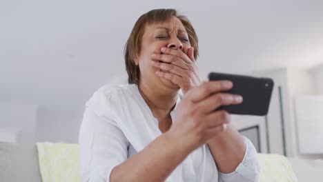 feliz mujer mayor afroamericana sentada en el sofá haciendo una videollamada usando un teléfono inteligente, riendo