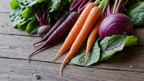 fresh carrots, beets, and greens on a wooden table