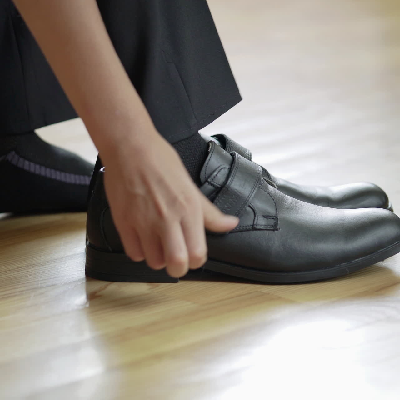 Boy is putting on new black shoes with the help of special object indoors. Classic leather shoes on velcro a male child puts on his feet with shoe spoon in the room.