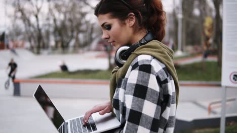 Ein-Ruhiges,-Schönes-Mädchen-Geht-Durch-Den-Park.-Mit-Einer-Hand-Hält-Sie-Einen-Laptop-Und-Schreibt-Jemandem-Nachrichten.-Trendiger-Look.-Zeitlupe