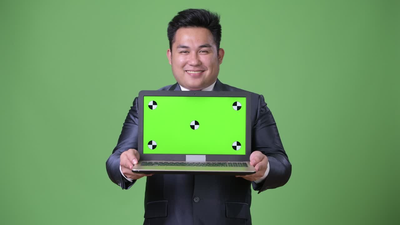 Young handsome overweight Asian businessman against green background