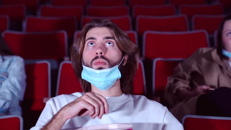 man watching a movie in the theater with a face mask on.