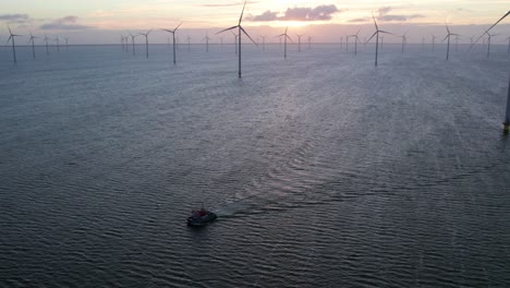 Barco-Que-Viaja-Frente-A-Altas-Turbinas-De-Viento-En-El-Parque-Eólico-Marino,-Amanecer