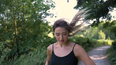 young woman jogging on a path in a park stops to answer a call on her cell phone