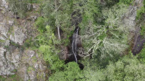 Aerial-view-looking-down-at-Cascata-do-Barbelote-woodland-waterfall-on-rocky-forest-path-slope-of-Monchique,-Portugal