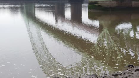 Plätschernde-Grüne-Gewölbte-Stahlträgerbrücke,-Die-Sich-Im-Langsam-Fließenden-Flusswasser-Widerspiegelt,-Das-Nach-Rechts-Schwenkt