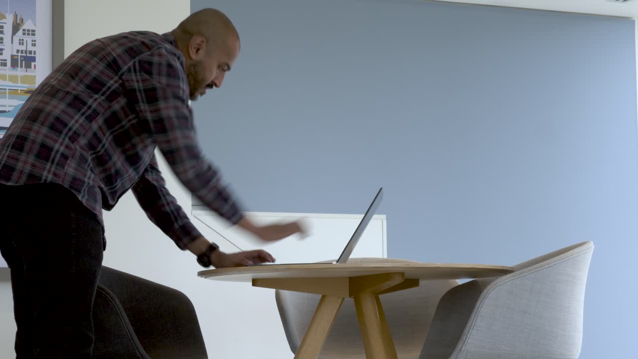 hombre de minoría étnica caminando hacia la mesa con una computadora portátil e iniciando sesión en un espacio de trabajo remoto