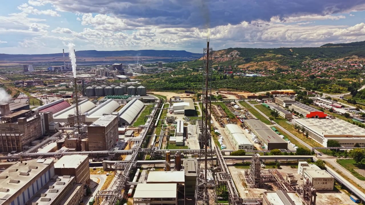 Gran zona industrial con fábricas, chimeneas y áreas verdes mostrando actividad diurna bajo un cielo azul.