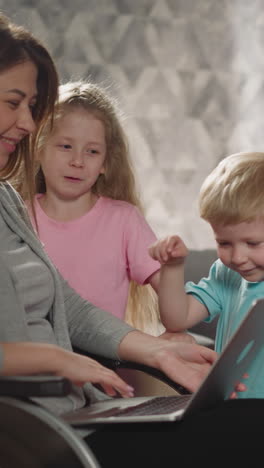 mother laughs letting children press buttons on modern laptop while working. caring woman with injury teaches little son and daughter to use gadget