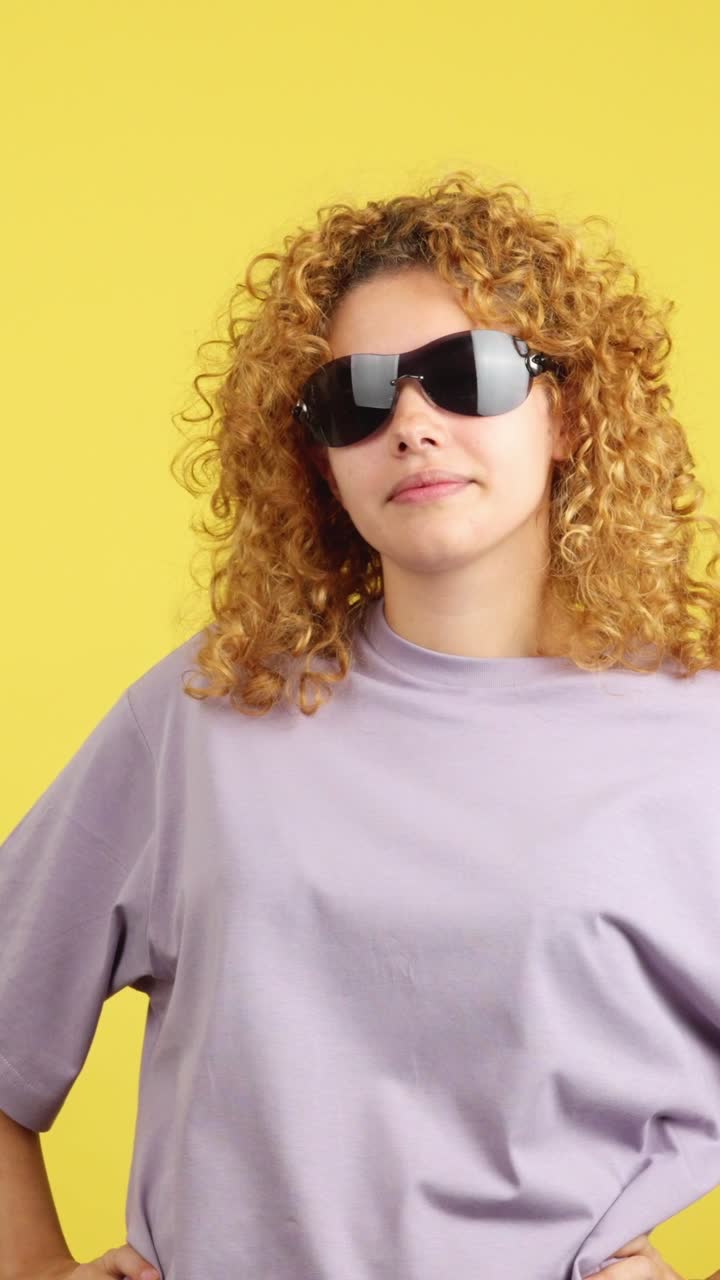 Young woman with curly hair posing in sunglasses on a yellow background