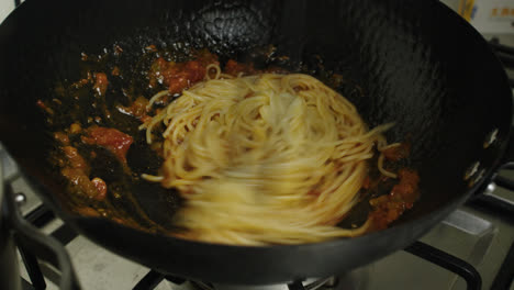 mixing pasta with bolognese sauce inside a frying pan