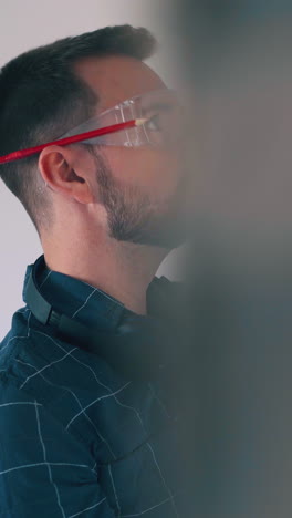 dolly cam shot: young bearded constructor in protective glasses checks wall angle with level at light empty room renewal