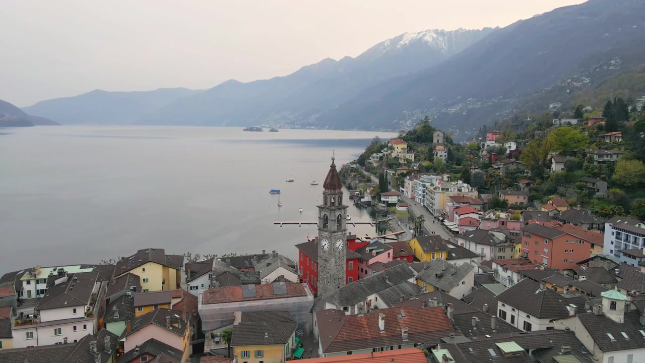Ripresa aerea di Ascona, Svizzera, che mostra case sul lungolago, colline e il Lago Maggiore sotto la torre dell'orologio.