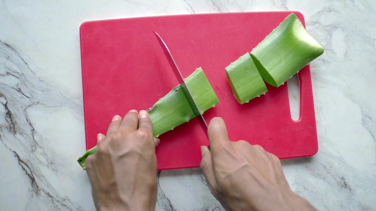 Seseorang Memotong Daun Lidah Buaya Segar di Atas Talenan Merah.