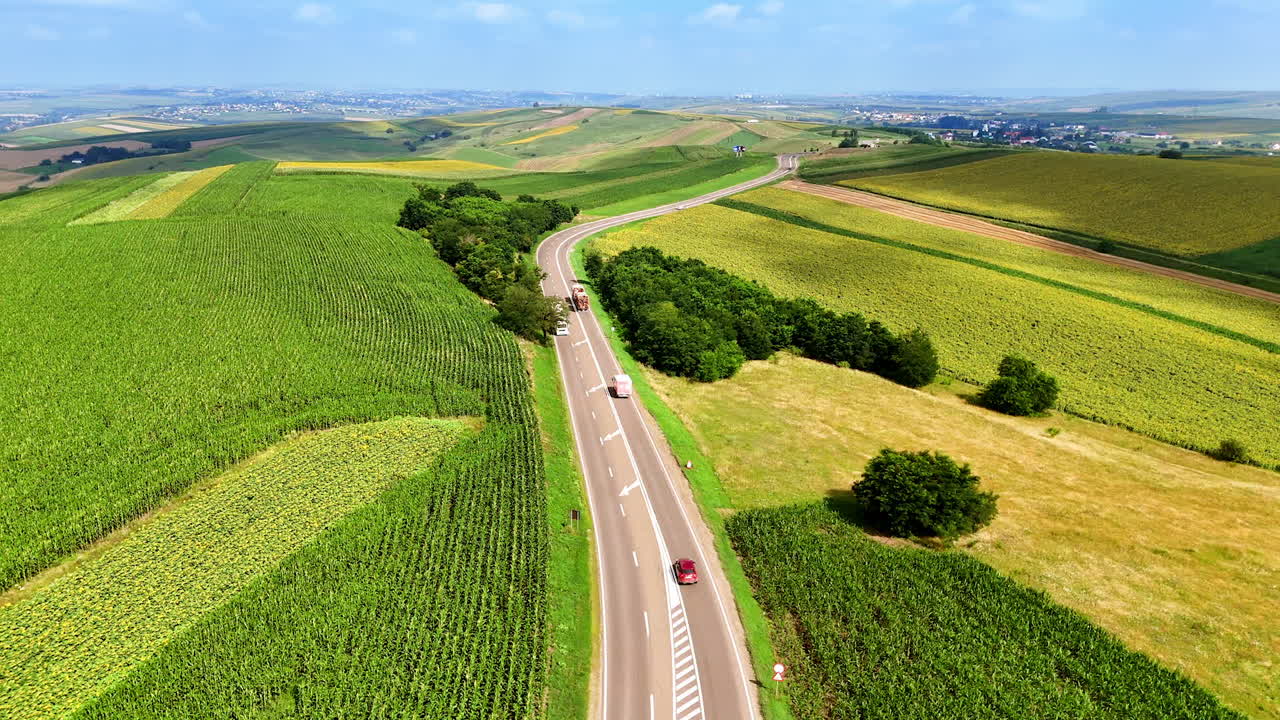 Scenic highway through lush green fields. A winding highway cuts through vibrant green fields under a clear blue sky. Trucks traverse the road