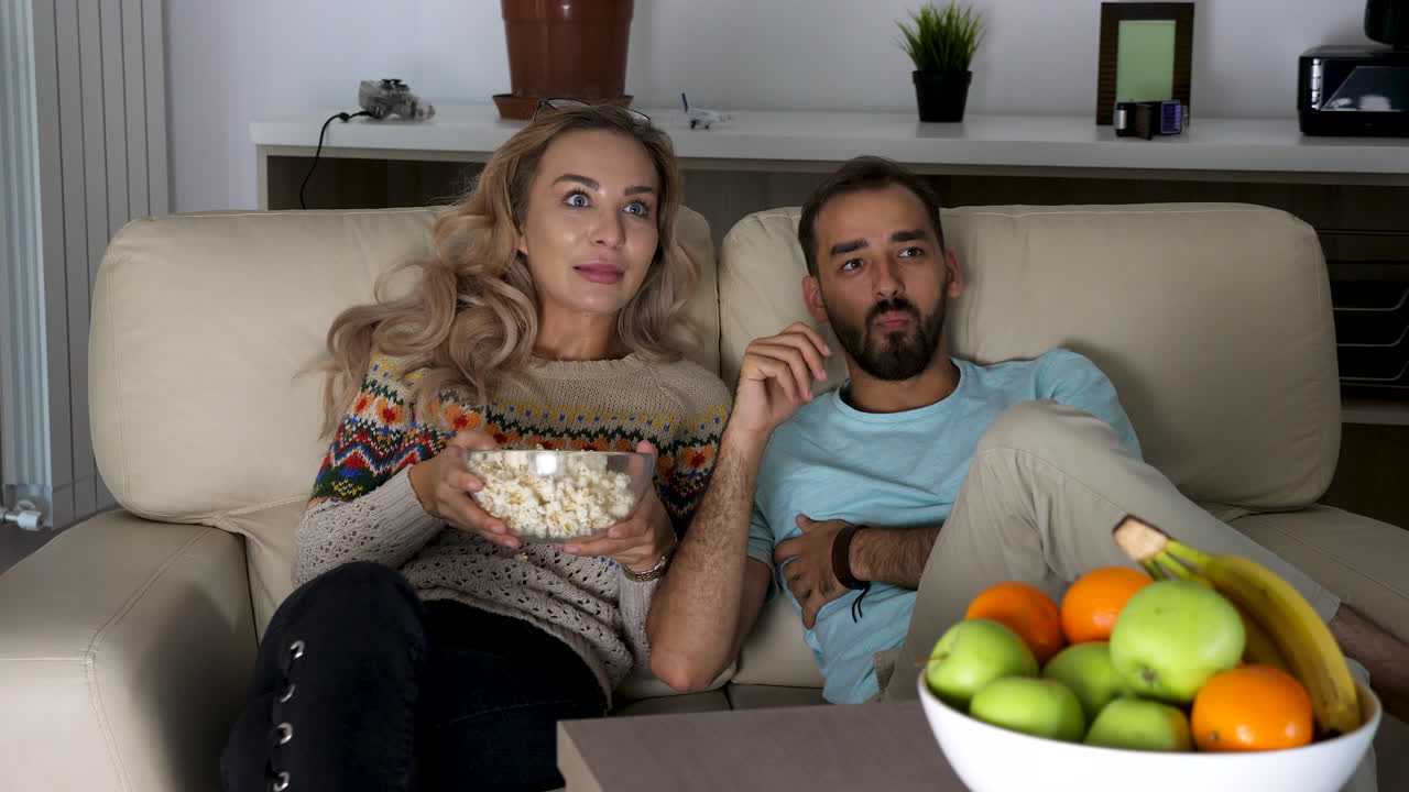 Couple watching TV with popcorn and fruits
