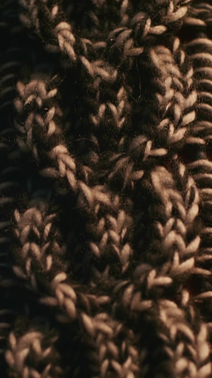 Vertical video: Drifting phone revealing two-tone cable knit sweater macro in room capturing fibers