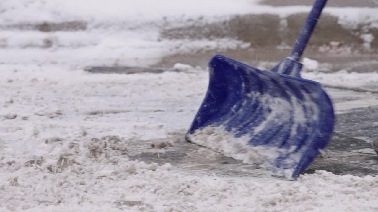 persona anónima limpiando la nieve de la calzada con una pala azul, cámara lenta
