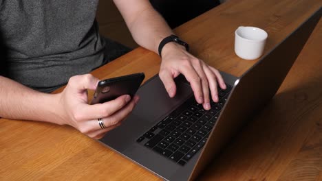 young hipster with smartwatch typing on laptop and scrolling on smartphone