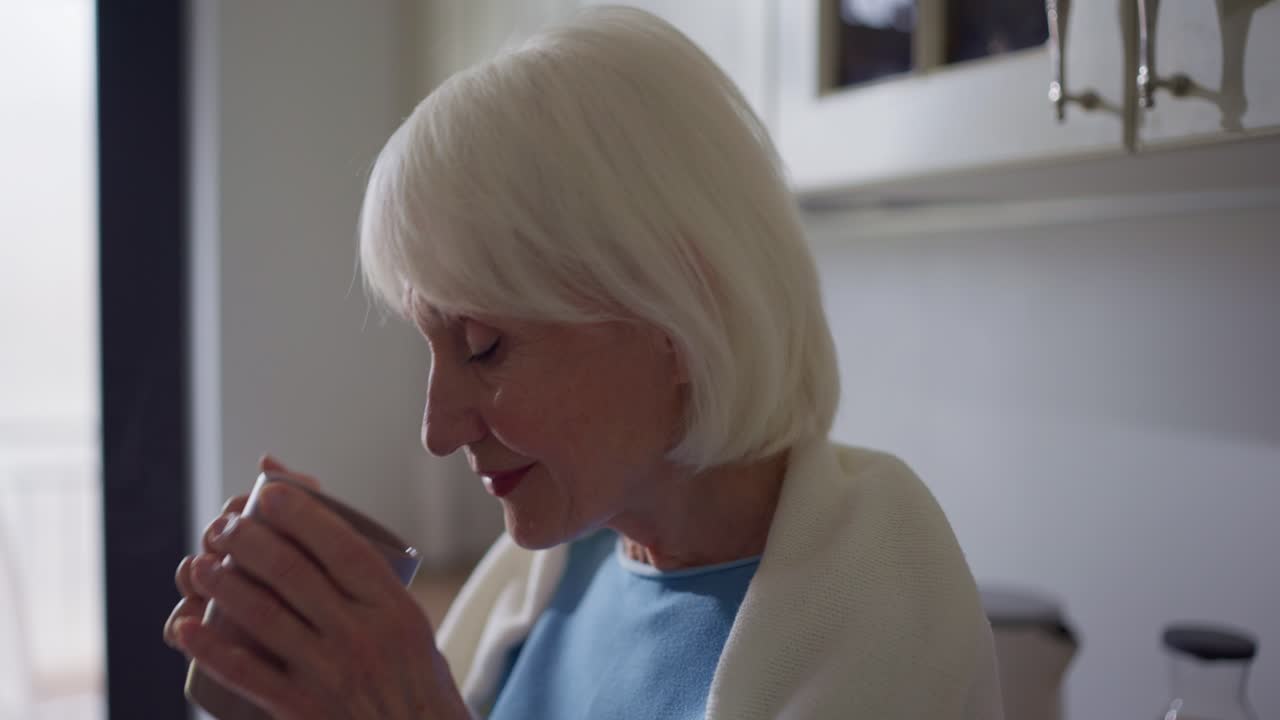 Elderly woman drinking from a mug in a kitchen