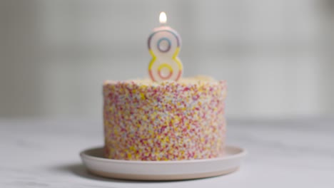 studio shot birthday cake covered with decorations and lit candle celebrating eighth birthday being blown out