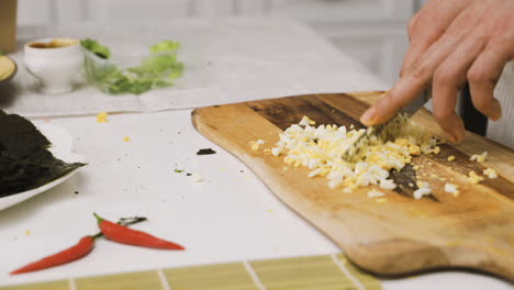 Close-Up-View-Of-Two-Hands-Chopping-Garlic-With-A-Knife-On-A-Kitchen-Board-On-The-Countertop