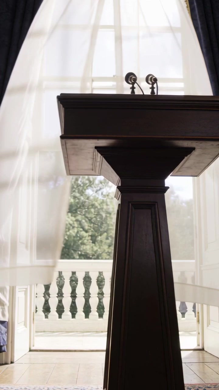 Vertical video: Billowing sheer curtains in hall, breeze moving lectern shadows and microphones