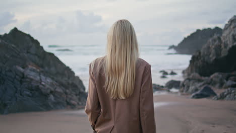 stylish lady stepping beach in suit back view. calm girl admiring rocky coast