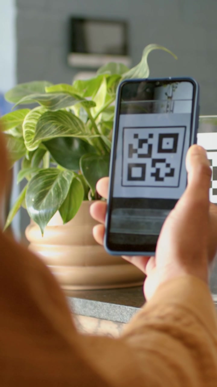 Vertical video: Tapping POS olive-apron cashier guiding man scanning QR to pay in cafe, copy space
