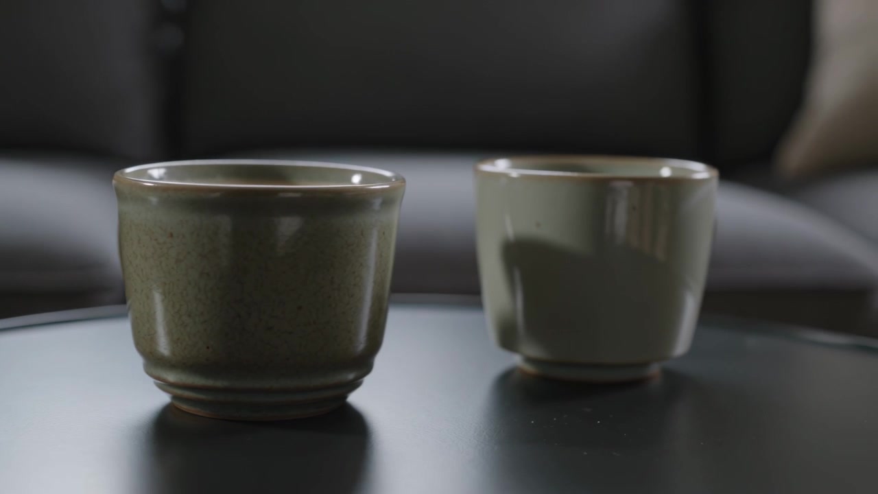 La telecamera si allarga rivelando due tazze di ceramica su un tavolino da caffè in salotto, inquadrando le tazze con il divano.