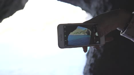 tomando una foto de una vista de la cueva del mar con un teléfono móvil