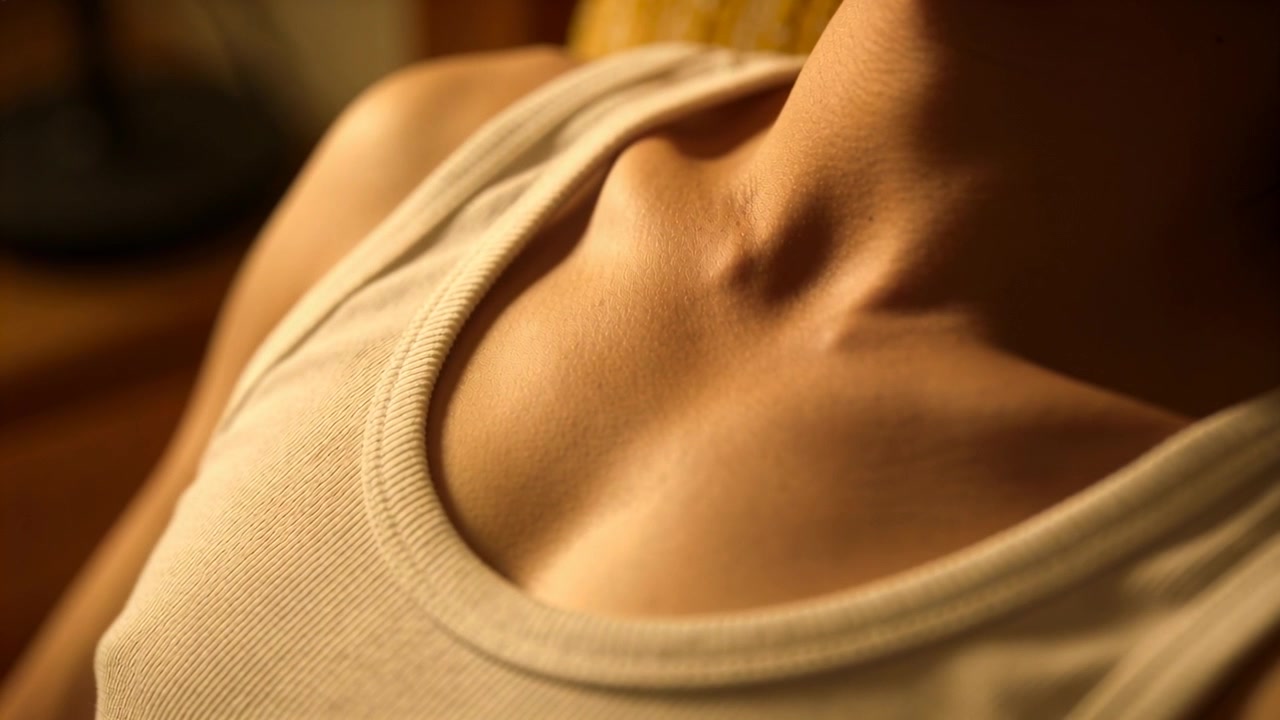 Donna che respira con una canotta bianca a costine, che inclina la testa in alto e a destra sul divano, rivelando le clavicole.
