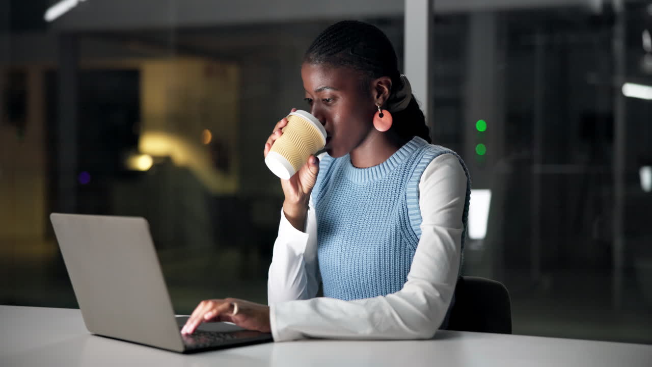 Young Black Woman Working on Laptop and Drinking Coffee in Office at Night