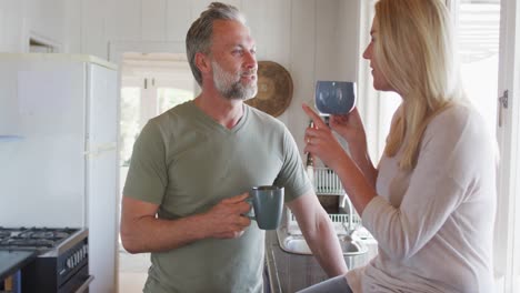 Relaxing-caucasian-mature-couple-drinking-coffee-and-talking-in-kitchen