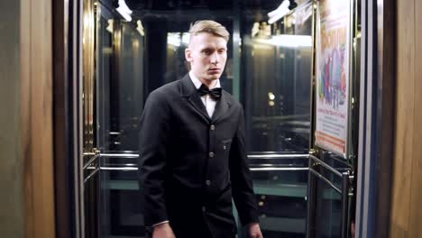 joven hombre de negocios en un traje negro entrando y ascensor con puertas de vidrio