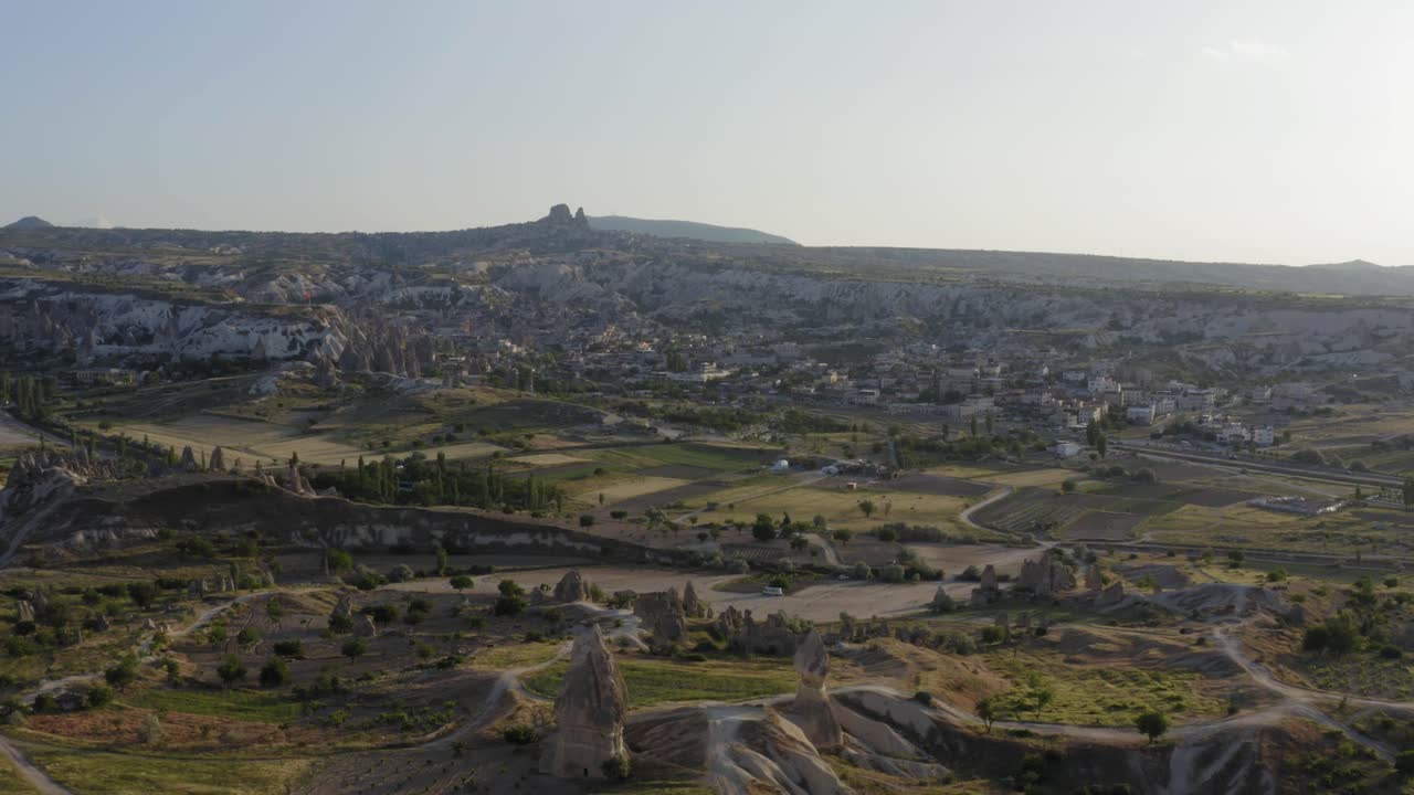 Panoramica con drone per una vista aerea su campi di erba verde nella valle con formazioni rocciose e montagne in Cappadocia, Turchia.