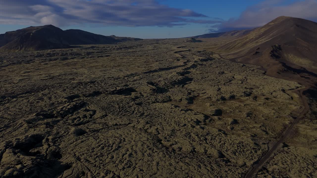 Estrada cênica atravessando um vale verde vibrante na Islândia. O vídeo destaca a beleza natural da Islândia com terreno musgoso exuberante, rios sinuosos e montanhas imponentes à distância.