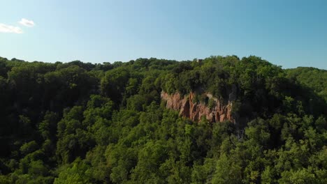 AERIAL-DOLLY-IN:-Drone-rising-on-top-of-a-green-valley,-with-summer-woodlands,-some-rocky-mountains-and-a-blue-sky,-Italy,-4k-aerial