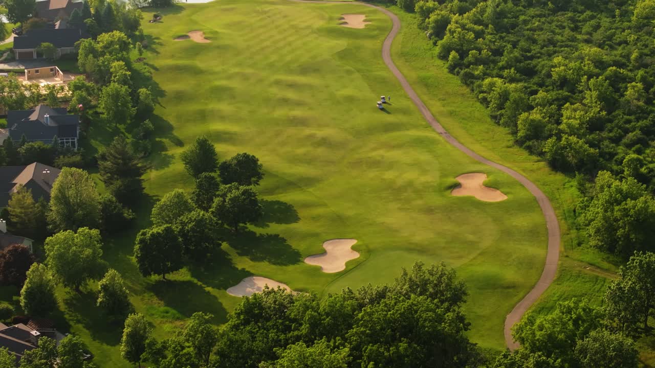 Golfers driving carts across golf course fairways and heading toward putting green at sunrise