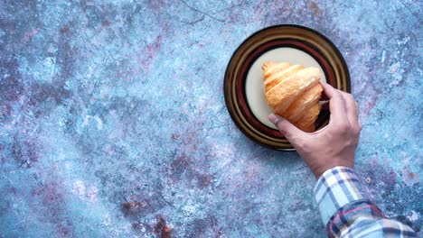 hand reaching for a croissant on a plate