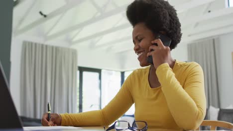 Glückliche-Afroamerikanische-Frau,-Die-Am-Tisch-Sitzt-Und-Auf-Dem-Smartphone-Spricht