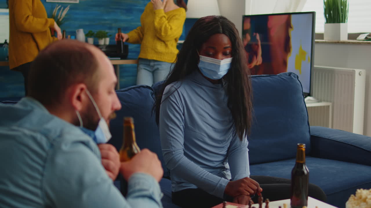 Diverse friends clinking bottles of beer playing chess at home