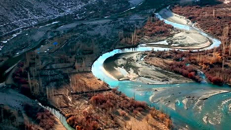 drone flying over turquoise winding river with sun reflected on surface in valley landscape of ghizer valley of gilgit baltistan