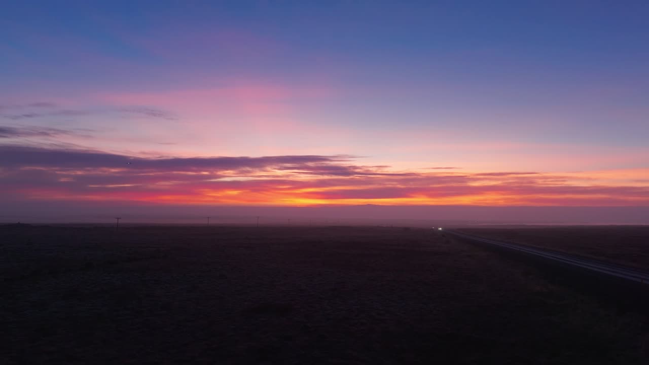 Fredfyldt tusmørke over et fladt landskab med levende orange og pink nuancer på himlen og en fjern runway som en vej ved solnedgang