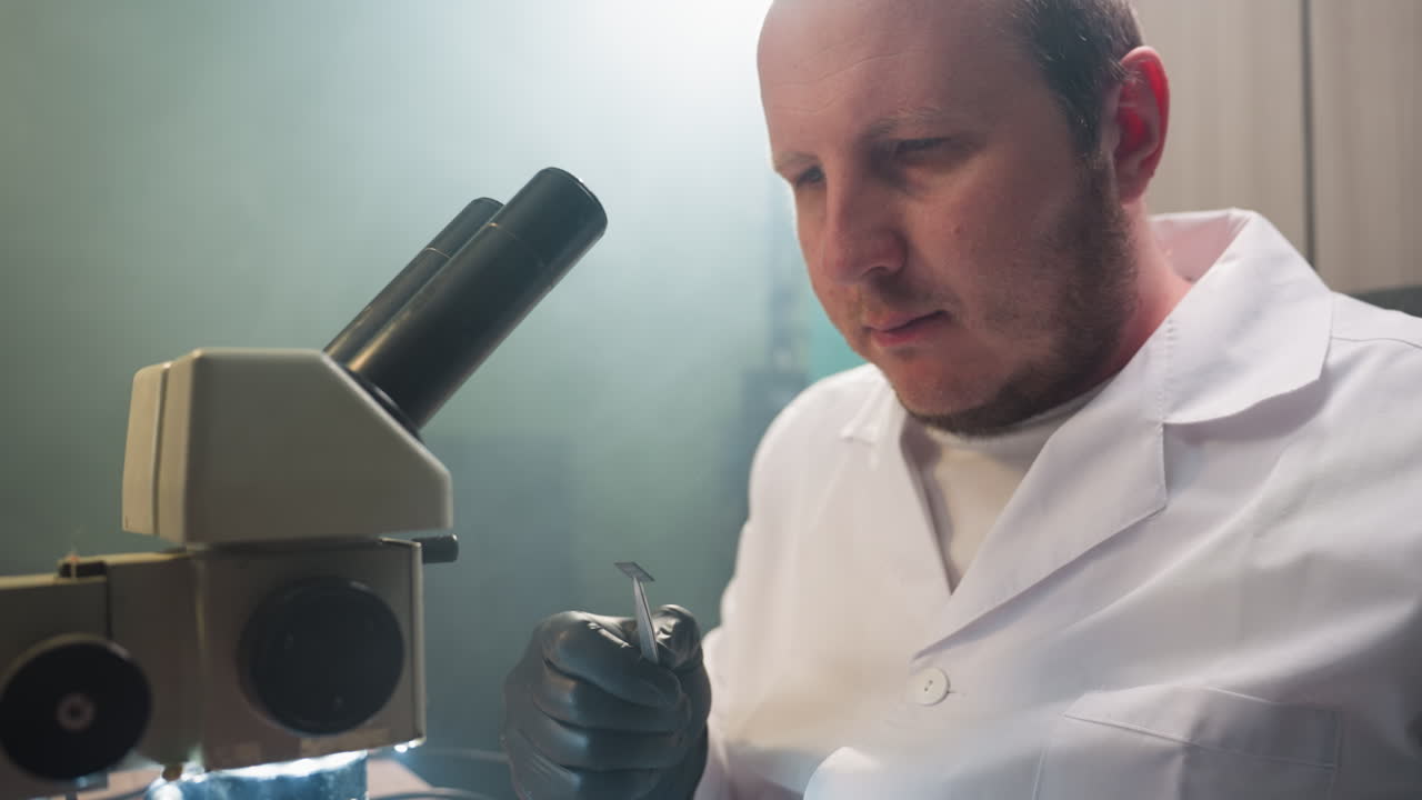 A close-up view of a focused technician in a lab coat examining a small electronic component under a microscope