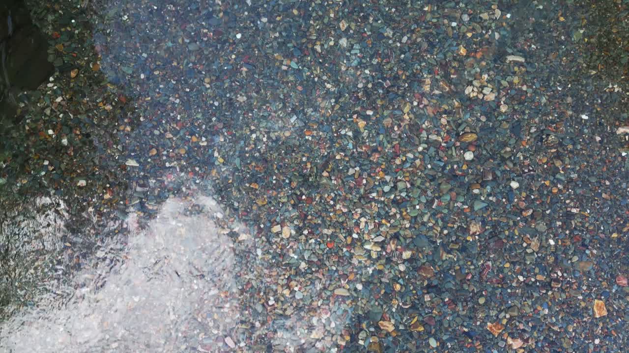 Drone top view of crystal clear freshwater revealing colorful stones and riverbed texture in natural swimming area in Extremadura Spain. Scenic summer travel background